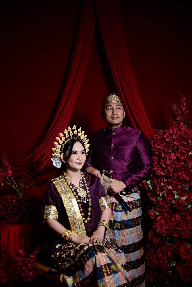 Iwan berdiri di samping Yuli yang duduk, mengenakan busana burgundy